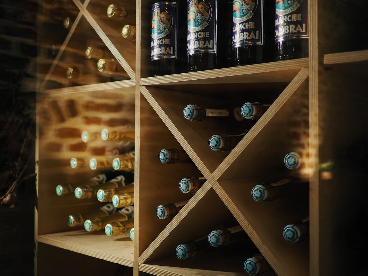 about-04 Wooden shelves in a wine cellar showcasing beer and wine bottles with a brick wall backdrop.